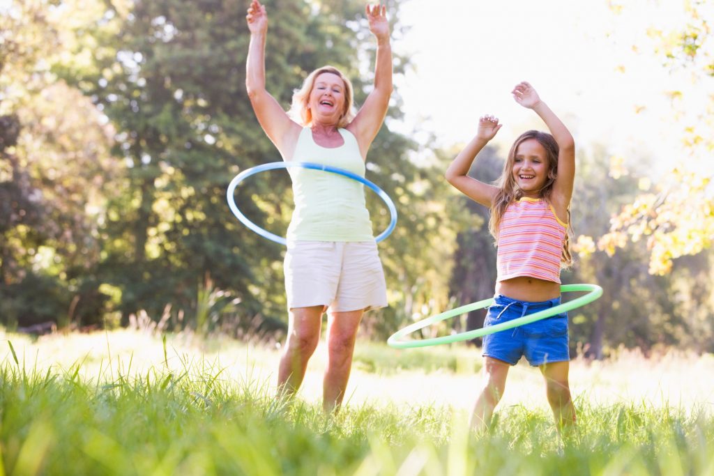 A girl and her grandmother are playing with hoola hoops outdoors