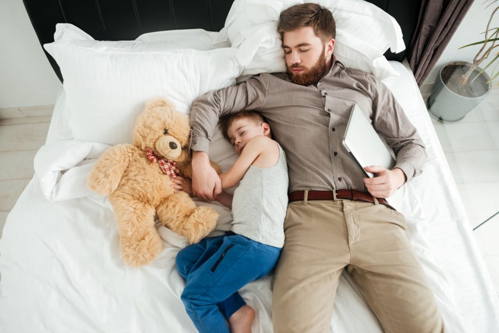 Little boy sleeping in bed with his father still fully dressed beside him